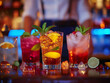 © Gayan - Assorted colorful cocktails on bar counter with bartender in background and vibrant lighting.