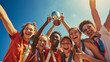group of joyful athletes is celebrating a victory, holding up a trophy against a clear blue sky