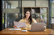© Wasana - Attractive Asian businesswoman working with laptop and checking documents at table in office.