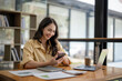 © Wasana - Attractive Asian businesswoman sitting using mobile phone at table in office