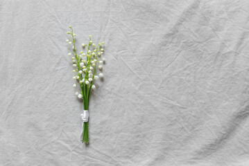 Wall Mural - Bouquet of white lily of the valley flowers on a light gray linen background. Women's or Mother's Day concept with white flowers on a plain background. Empty card for congratulations, copy space.