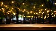 Empty wood table top with decorative outdoor string lights hanging on tree at night
