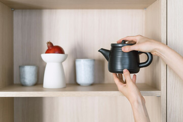 Wall Mural - Female hands taking ceramic teapot from wooden shelf for prepare tea