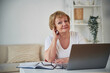 © standret - Front view. Sitting by table with laptop. Senior elderly woman is at home in the living room