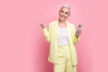 Photo of successful businesswoman suit point finger empty space using smartphone application for planning isolated on pink color background