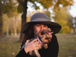 Beautiful stylish elegant joyful woman in a large hat and black coat portrait with a small Yorkie dog in her arms
