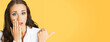 © vgstudio - Portrait image of excited surprised shocked astonished businesswoman pointing away side with finger. Business woman covering open mouth by her hand. Isolated yellow background. Wide banner composition