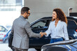 © Dragana Gordic - Happy salesman congratulating his female customer for buying a new car in a showroom. Salesperson selling cars at car dealership.