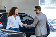 © Dragana Gordic - Happy salesman congratulating his female customer for buying a new car in a showroom. Salesperson selling cars at car dealership.