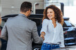 Happy salesman congratulating his female customer for buying a new car in a showroom. Woman buying a new car in car dealership. Handshake and good deal