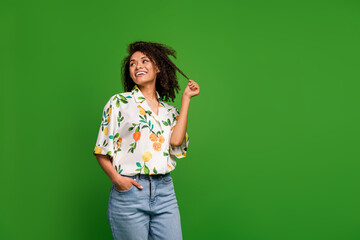 Wall Mural - Photo of shiny sweet woman dressed print shirt looking empty space holding hair curl isolated green color background