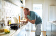 © Marko Geber - Middle aged man cooking in home kitchen with laptop