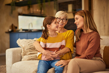 Canvas Print - A little girl sitting in her grandma's lap while looking at her mother, spending time together, at home.