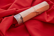 A Gift Wrap Tied With A String On A Red Fabric Background. Dollar Bills Peek Out Of The Fabric