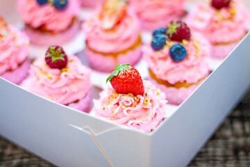 Festive pink cupcakes with fresh strawberries, raspberries and blueberries on cardboard box with chopped pistachios on the top