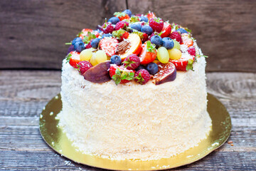Wall Mural - Coconut cake with a pile of fresh peaches, apples, raspberries, blueberries and nuts on wooden background