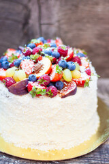 Wall Mural - Coconut cake with a pile of fresh peaches, apples, raspberries, blueberries and nuts on wooden background