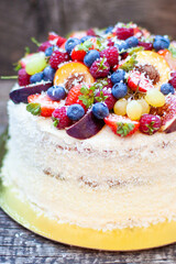 Wall Mural - Coconut cake with a pile of fresh peaches, apples, raspberries, blueberries and nuts on wooden background