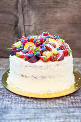 Wall Mural - Coconut cake with a pile of fresh peaches, apples, raspberries, blueberries and nuts on wooden background