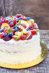 Wall Mural - Coconut cake with a pile of fresh peaches, apples, raspberries, blueberries and nuts on wooden background