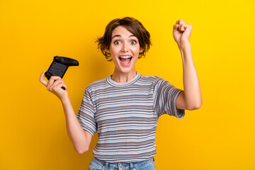 Wall Mural - Photo of ecstatic satisfied woman dressed striped t-shirt raising up playstation joystick win game isolated on yellow color background