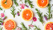 Top view of sliced oranges, grapefruits, sprigs of rosemary and small pink flowers arranged artistically on a white background. 