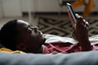 African American man with smartphone lying on couch in front of camera and watching online video or communicating with someone