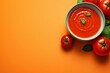 Bowl of tomato soup on orange background with fresh tomatoes, top view, copy space