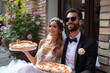 © Pinklife - A newlywed couple shares a slice of happiness as they enjoy a delicious pizza in their elegant wedding attire surrounded by blooming flowers