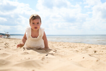 A portrait of a 1 year old caucasian baby girl on the sandy beach on a sunny warm day at Baltic Sea