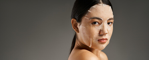 Wall Mural - banner, young asian woman with facial mask for skin treatment looking at camera on grey background