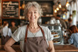 © samael334 - Portrait of smiling happy senior woman standing in her restaurant. Cheerful middle aged waitress wearing casual apron serves clients in restaurant