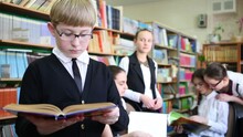 Five Schoolchildren In Library - Boy Reading A Book, Girls In The Background