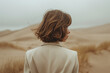 anonymous female with a bob haircut in a cream blazer, back to the camera, against soft dune contours