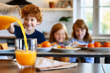 Selective Focus On Orange Juice Pouring From Jug Into Glass With Little Children In Background