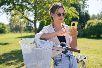 Wall Mural - European young woman in park with bicycle and talking on mobile phone