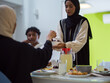 © .shock - A woman in a hijab extends a platter of dates to her diverse family, creating a scene of unity and joy as they come together to break their fast during the holy month of Ramadan, symbolizing the