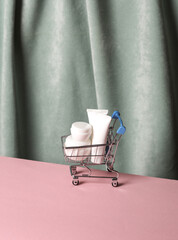 Wall Mural - Shopping trolley with Cream tubes against the background of curtain. Aesthetic beauty still life. Minimalism.