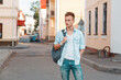 © alones - stylish cool American man with a hairstyle in fashion denim clothes with a backpack walks in the city. Student guy traveling