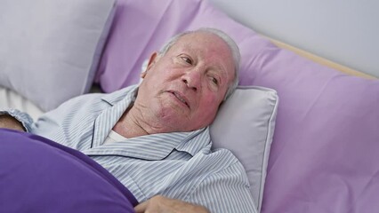 Canvas Print - Joyful senior man in stylish pyjamas sits confidently on bed, cool smile lighting up his mature face – personifying positive lifestyle in a cozy bedroom environment.