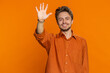 Young Caucasian man smiling friendly at camera, waving hands gesturing hello greeting or goodbye welcoming with invitation hospitable expression. Handsome guy isolated on orange studio background