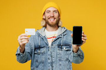 Young man in denim shirt hoody beanie hat casual clothes using blank screen mobile cell phone hold credit bank card do online shopping order delivery booking tour isolated on plain yellow background