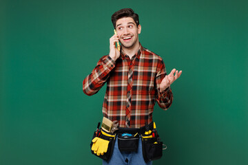 Wall Mural - Young happy employee laborer handyman man wear red shirt talk speak on mobile cell phone isolated on plain green background. Instruments accessories for renovation apartment room. Repair home concept.