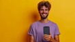 Explore a lifestyle moment as a smiling young man, donned in a purple t-shirt, proudly exhibits a smartphone with a big blank screen and gives a thumbs-up on a plain yellow background.