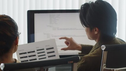 Back view of two programmers discussing tasks of clients project about software developing sitting in front of computer