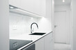 A Modern, bright kitchen with white cabinets, marble countertops, and a sleek sink under minimalist lighting.