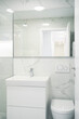 A Modern, bright bathroom with white marble walls, a glass shower, a sleek sink and cabinet, and a wall-mounted toilet.