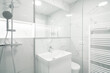 A Modern, bright bathroom with white marble walls, a shower, sink, toilet, and a heated towel rack. It has a clean and minimalist design.