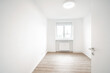 A Bright, spacious room with white walls, a wooden floor, a window, and a ceiling light. It’s clean and appears to be empty.