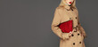 © Beauty Agent Studio - Cropped full body portrait of a fashionable young model posing against grey background dressed in trench coat and holding stylish red bag. Autumn fashion concept